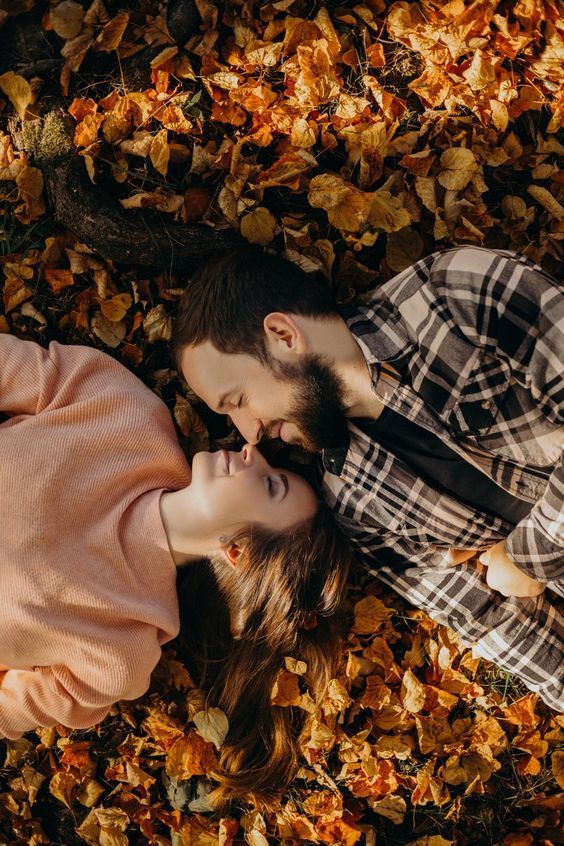 a man and woman laying on the ground surrounded by leaves