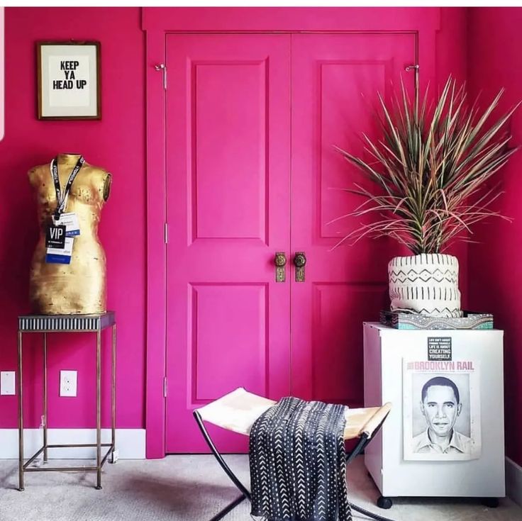 a room with pink walls and pictures on the wall next to a chair in front of a red door