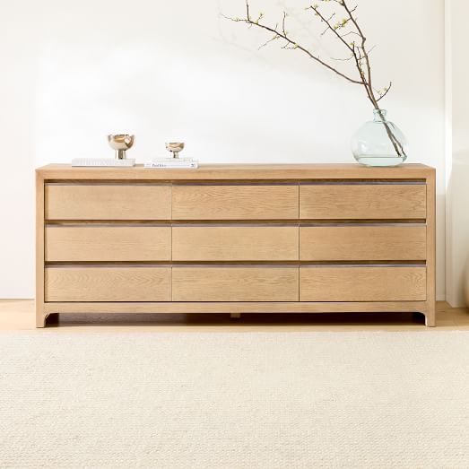 a large wooden dresser sitting next to a vase with flowers in it on top of a carpeted floor