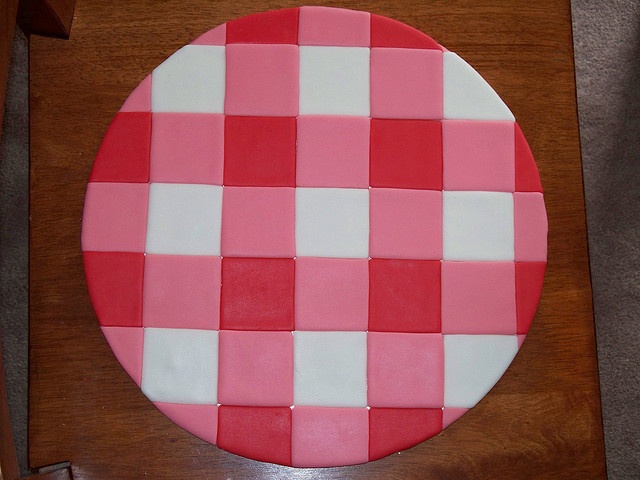 a pink and white checkered cake sitting on top of a wooden table