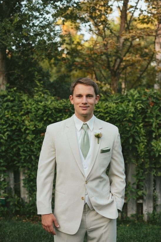 a man in a white suit and green tie posing for the camera with his hands in his pockets