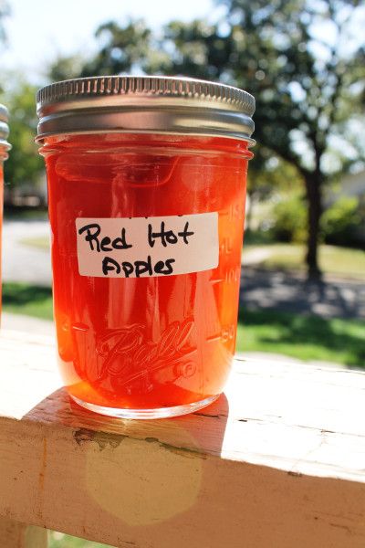 two jars filled with red hot apples sitting on top of a wooden table