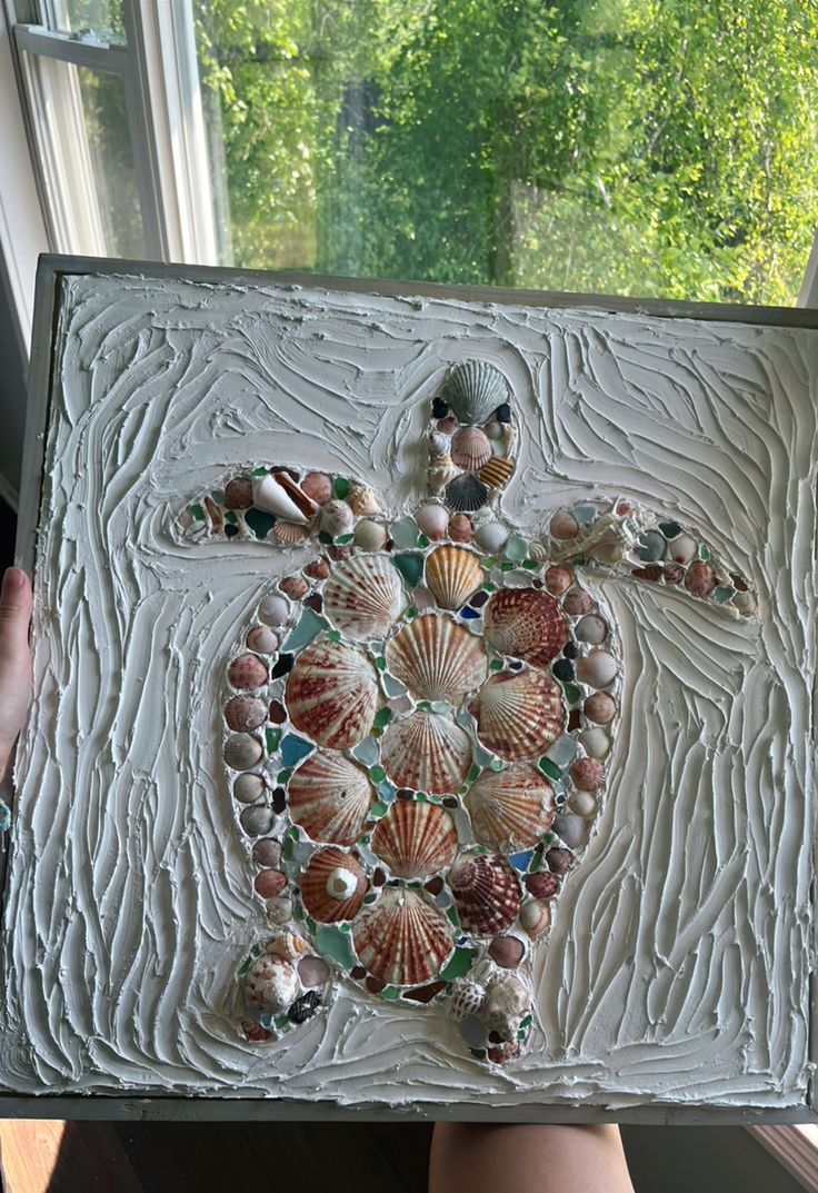 a sea turtle made out of seashells is displayed in front of a window