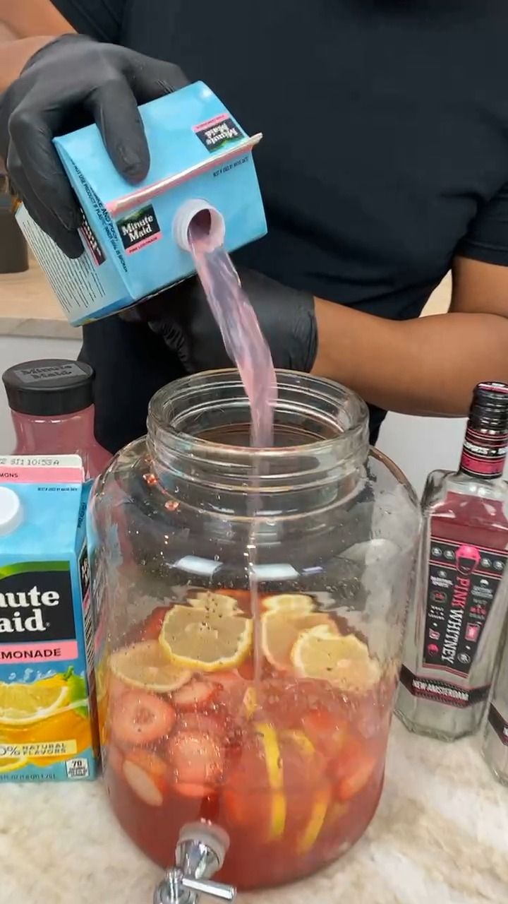 a person pouring liquid into a jar filled with lemons and strawberries in it