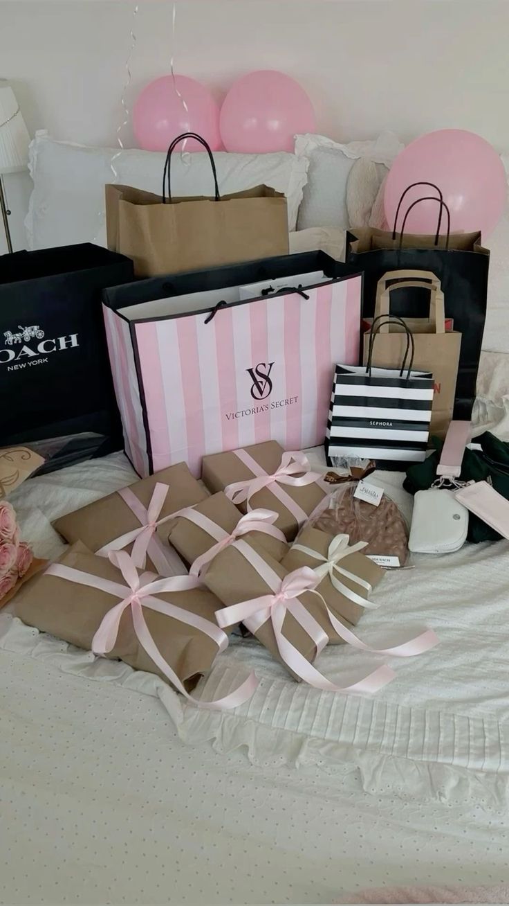 several bags and gifts on a bed with pink balloons in the background, some are wrapped in brown paper