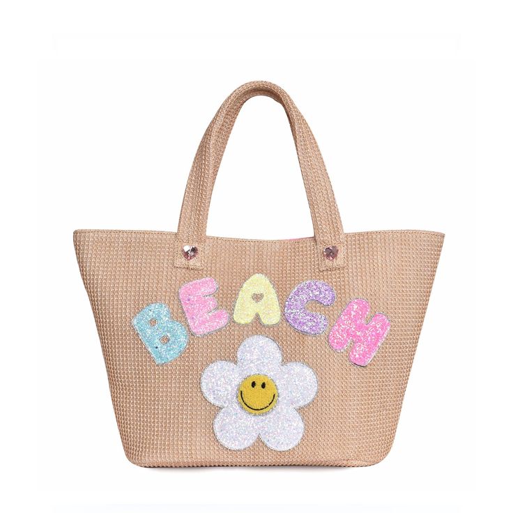 Front view of straw 'Beach' tote bag with glitter daisy and bubble-letter patches Trendy Crochet Bag With Braided Handles For Beach Season, Trendy Straw Bag With Braided Handles For Vacation, Top Handle Straw Beach Bag, Top Handle Beach Vacation Bags, Trendy Woven Tote Beach Bag, Chic Vacation Beach Bag With Top Handle, Trendy Jute Beach Bag For Vacation, Chic Sand Colored Beach Bag For Spring, Top Handle Bags For Beach Vacation