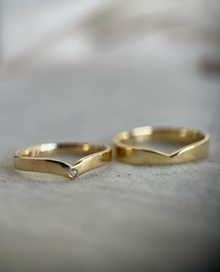 two yellow gold wedding rings sitting on top of a bed