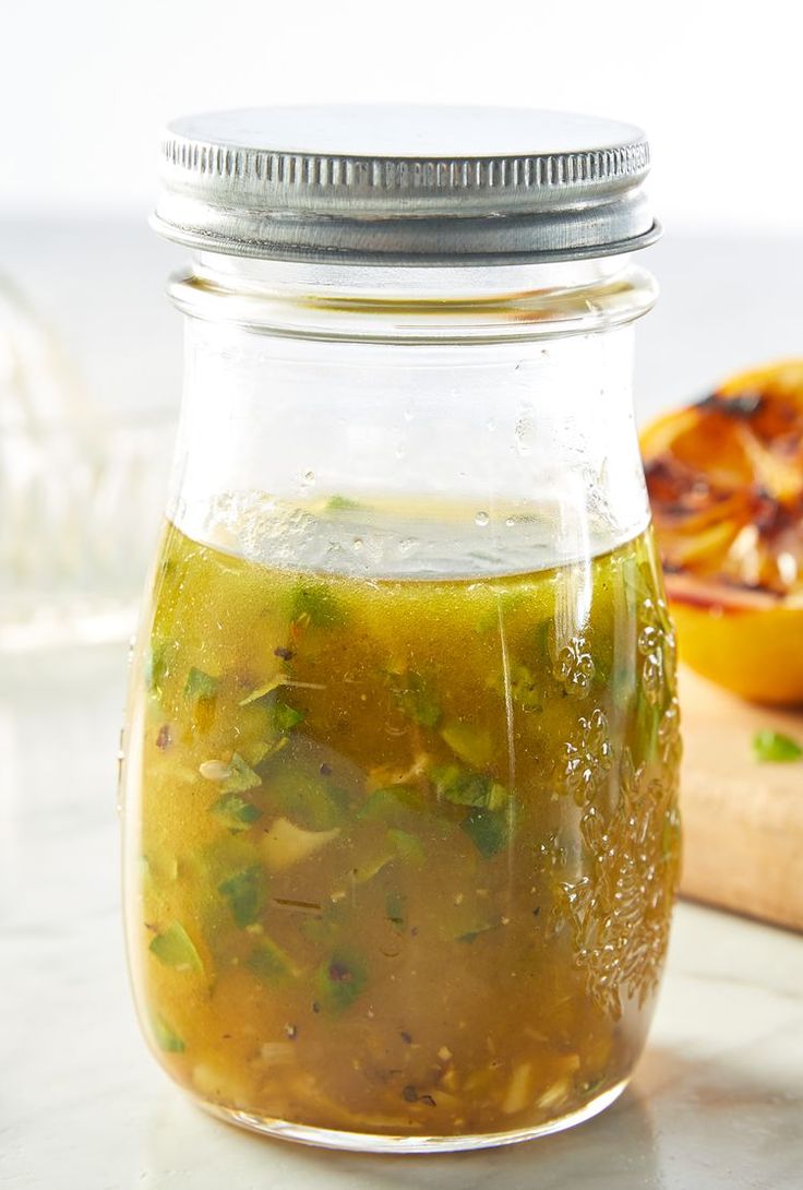 a jar filled with green liquid sitting on top of a counter next to an orange