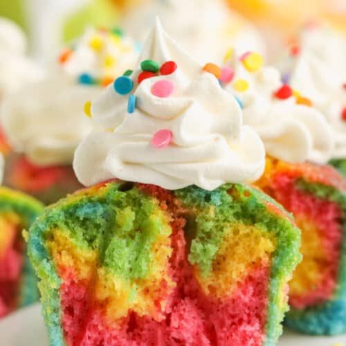 rainbow cupcakes with white frosting and sprinkles are on a plate