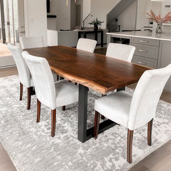 a dining room table with white chairs and an area rug on the floor in front of it