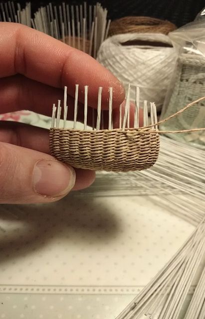 a person is holding a small piece of wood with pins in it and some yarn on the table