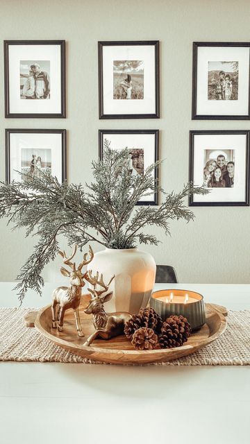 a tray with pine cones and candles on top of a table next to framed pictures