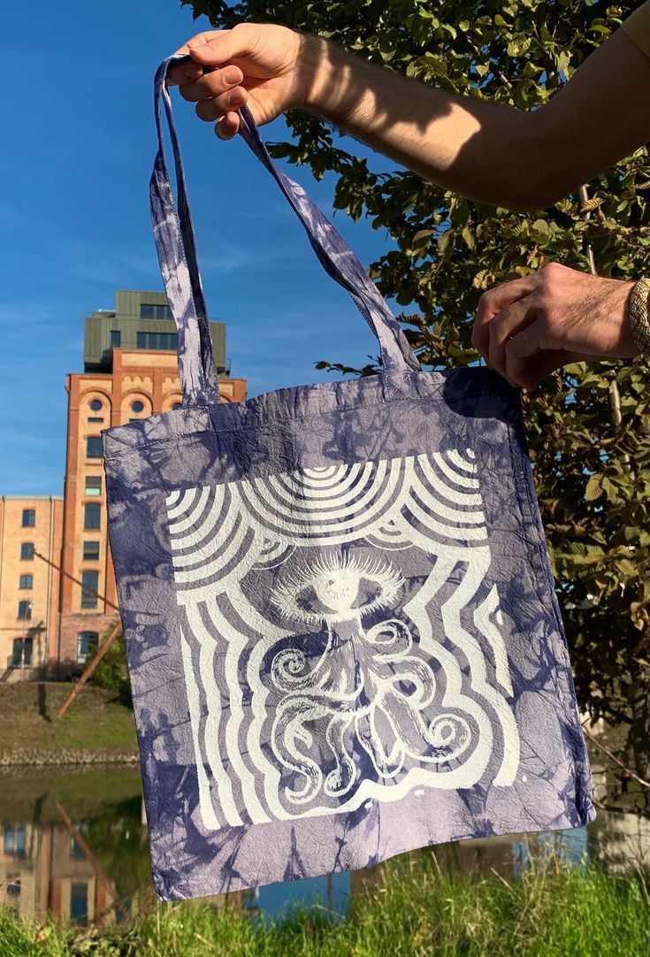 a person holding a bag with an image on it in front of some trees and buildings