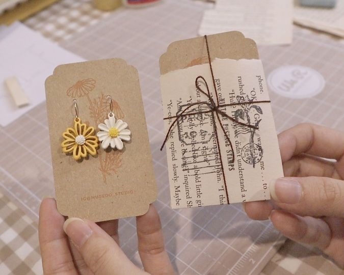 two small tags with flowers on them being held by someone's hands at a table