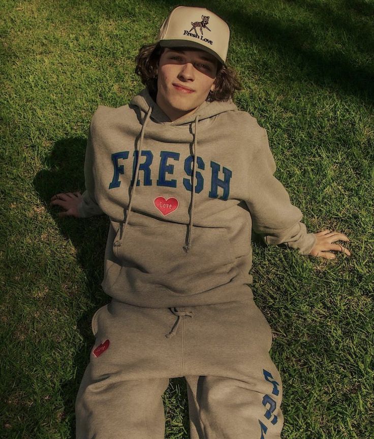 a young boy laying in the grass wearing a hoodie and sweatpants with writing on it