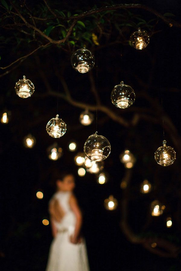 a bride standing under a tree with lights hanging from it's branches in the dark