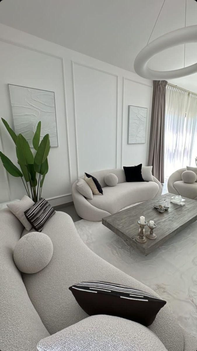 a living room filled with white furniture next to a tall plant in a vase on top of a table