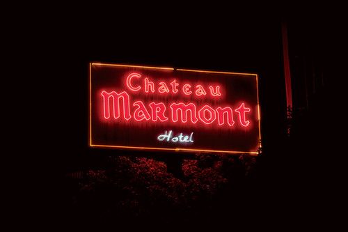 a neon sign that says chateau marmont hotel in the dark with trees behind it