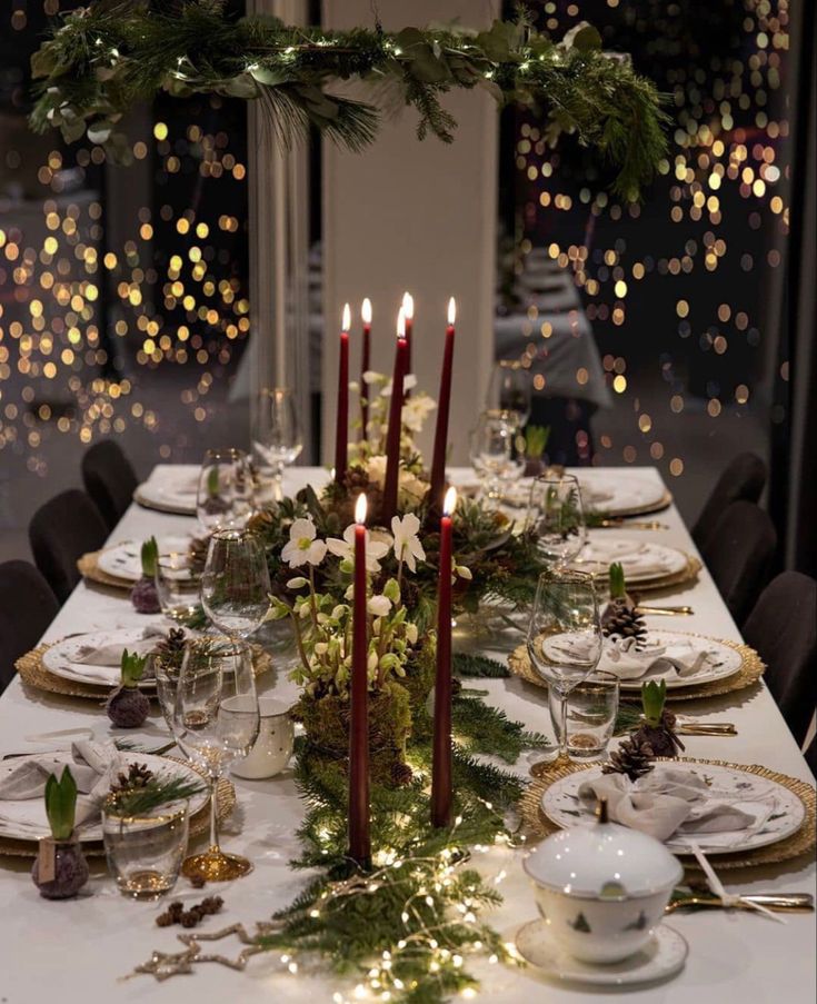 a table set for christmas with candles and greenery