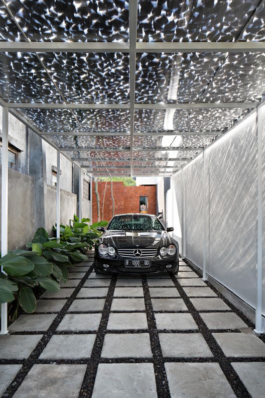 a car is parked in the middle of a walkway with plants on both sides and an awning over it