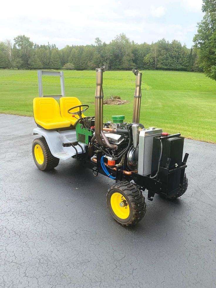 a small tractor with two large tires parked in a parking lot next to a green field