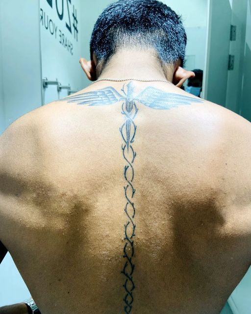 the back of a man with a tattoo on his upper and lower back, in front of a mirror