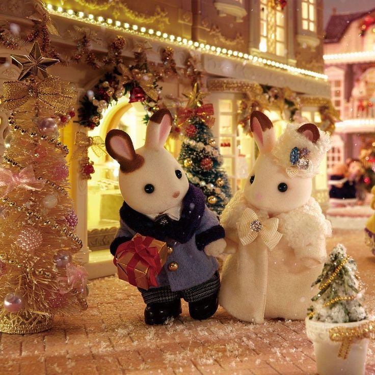 two stuffed animals sitting next to each other in front of a christmas tree and building