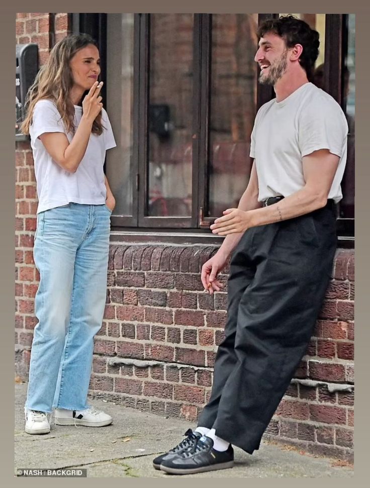 a man standing next to a woman on the side of a brick building with her hand in her mouth