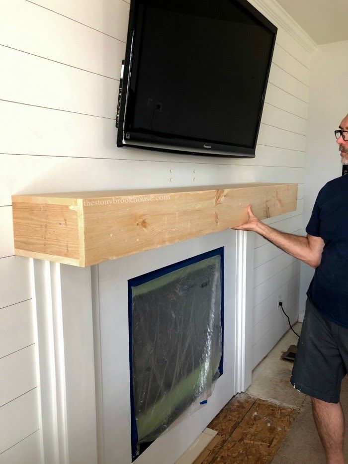 a man standing in front of a flat screen tv mounted on a wall above a fireplace