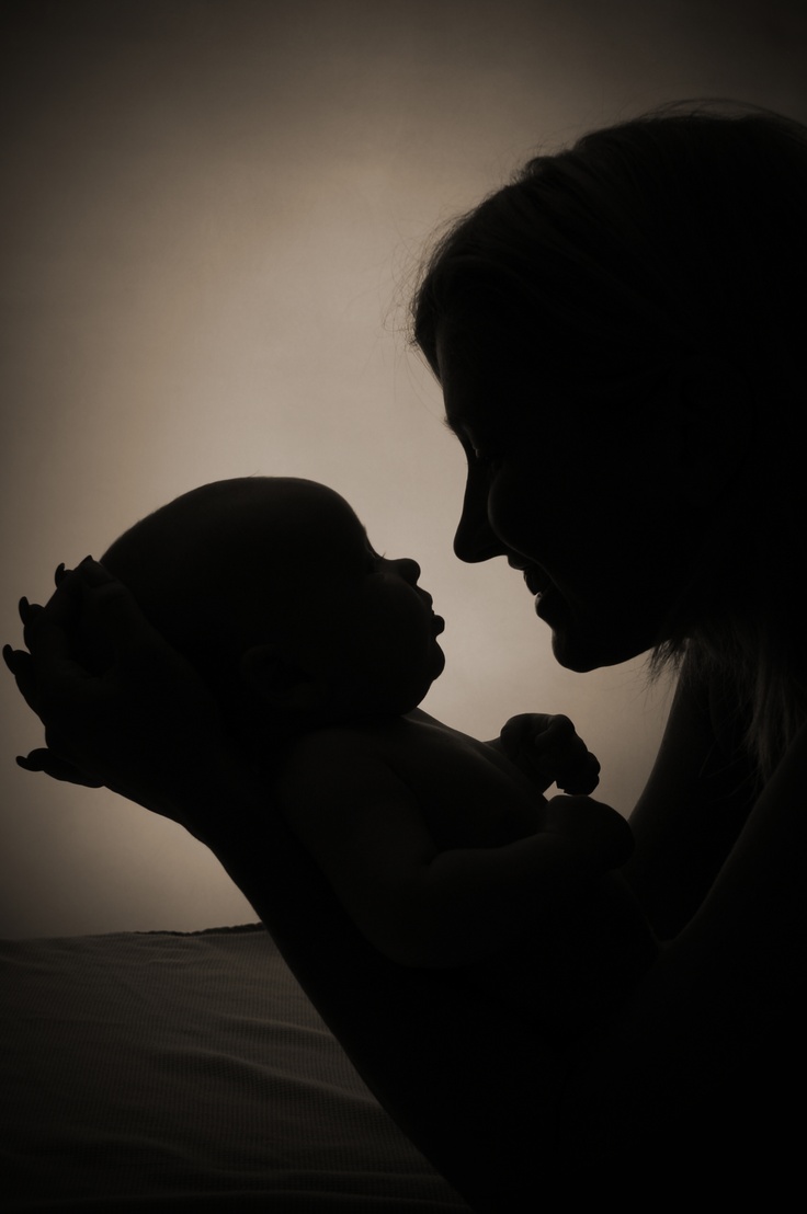 a woman holding a baby in her arms with the light shining on her face and head