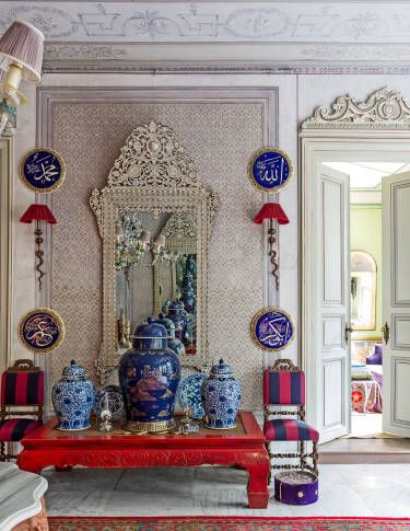 an ornately decorated room with blue and white vases on a red table in front of a mirror