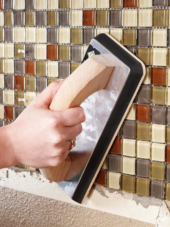 a person using a wooden spatula to remove glass from a tabletop in front of a mosaic tile wall