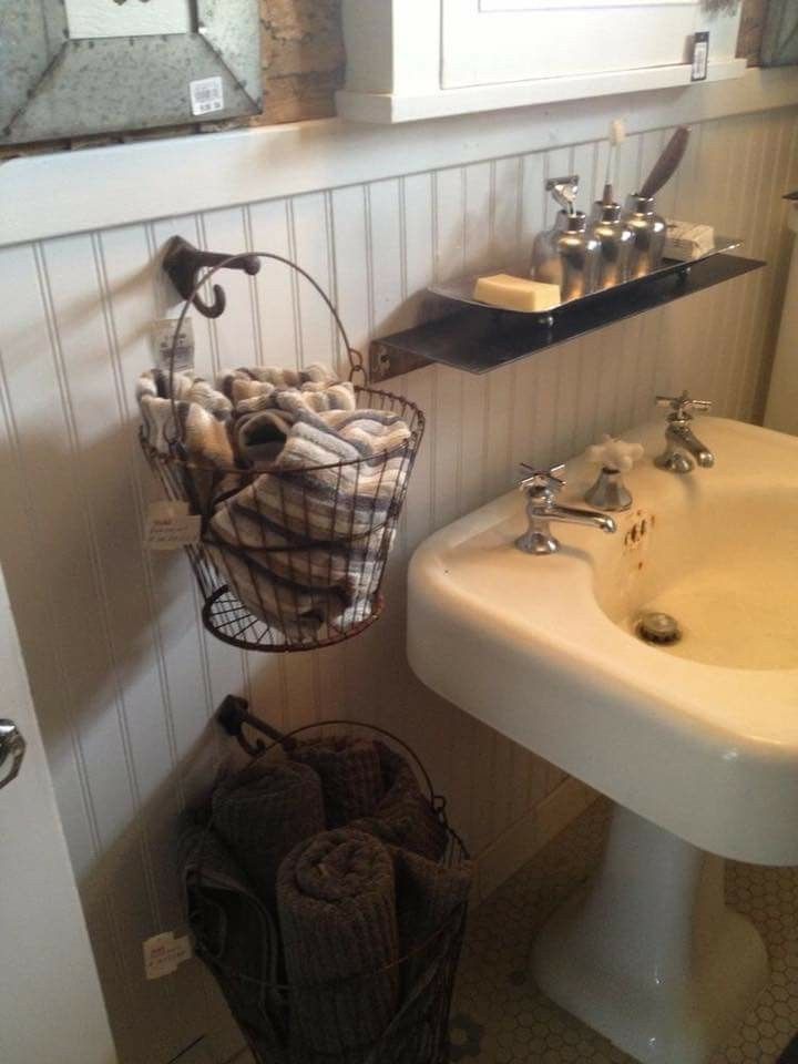 a white sink sitting next to a mirror in a bathroom under a hanging basket filled with towels