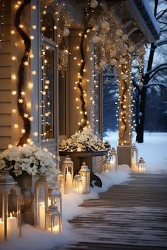 lighted lanterns are on the front porch of a house with flowers and trees in the snow