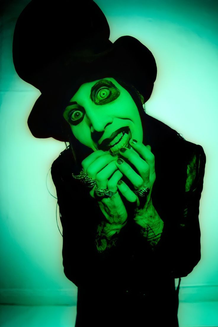 a man with green makeup and black hat holding his hands to his mouth while wearing a top hat