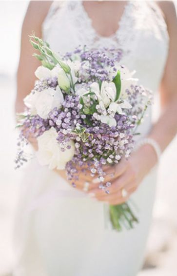 the bride is holding a bouquet of lavenders and white flowers in her hands, while she wears a wedding dress