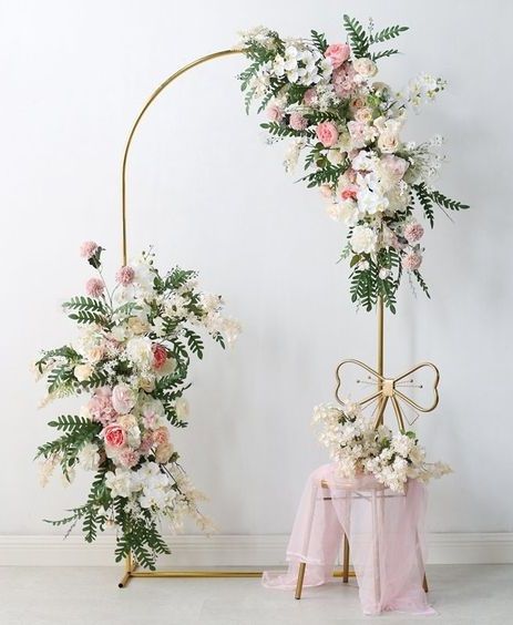 two floral arrangements on display in front of a white wall and pink chair covers with bows