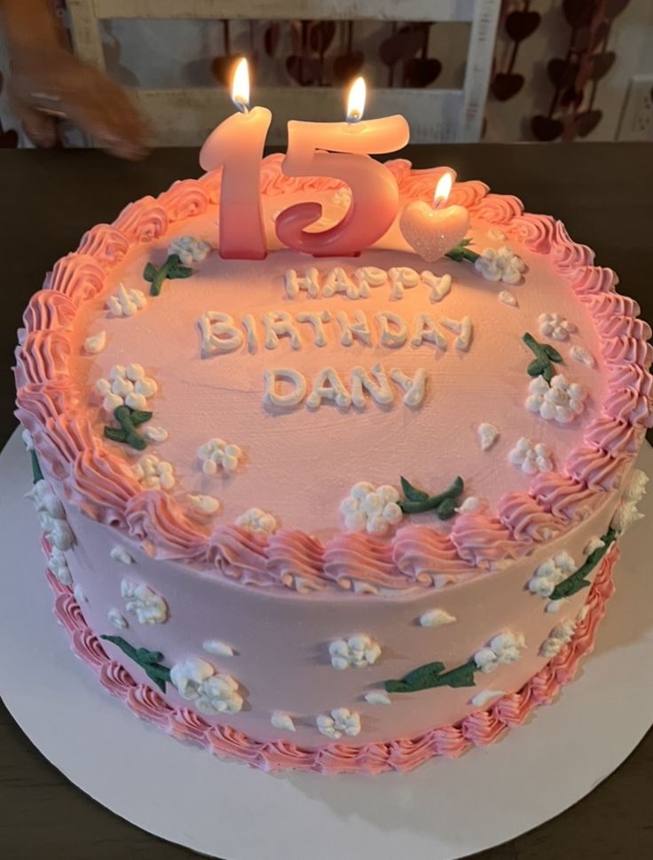 a birthday cake with pink frosting and lit candles on top that reads, fifteen happy birthday day