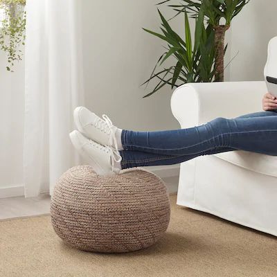 a woman is sitting on a bean bag chair and reading a book in her living room