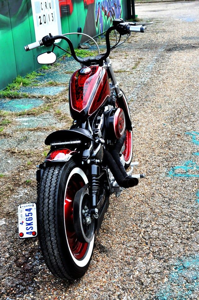 a red and black motorcycle parked in front of a green wall with graffiti on it