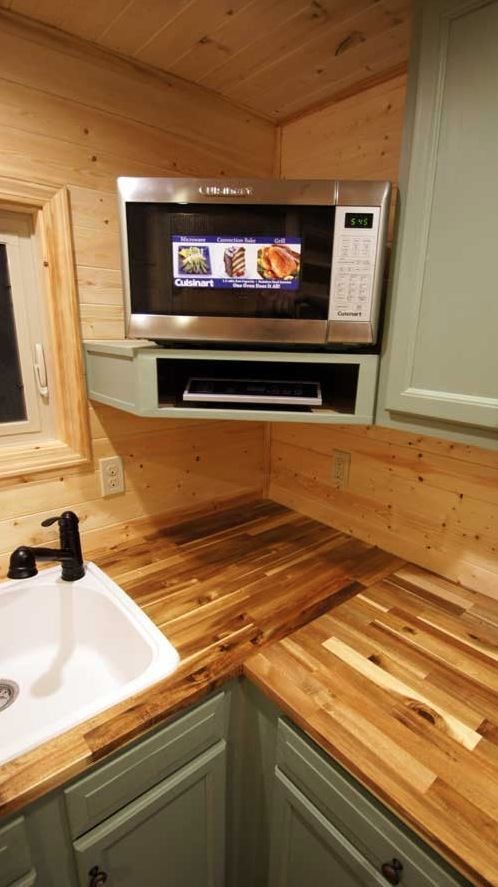 a kitchen with wooden counter tops and green cabinets, including a microwave above the sink