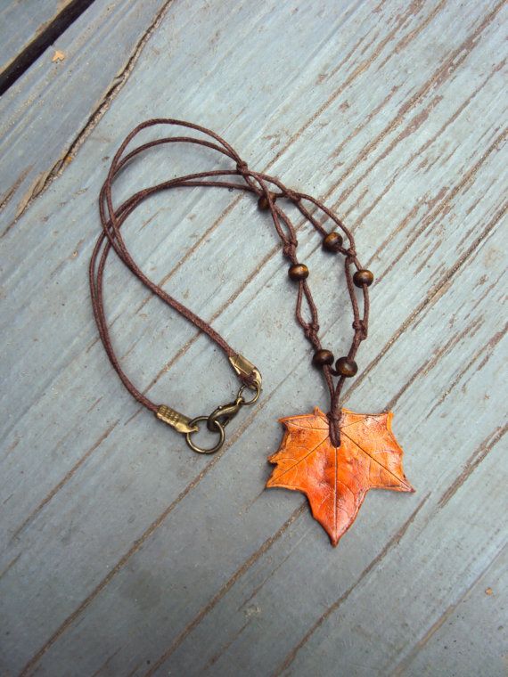 an orange leaf is hanging from a brown cord on a wooden surface with a brass chain