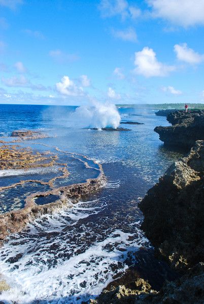 the water is splashing out of the rocks into the ocean and blue skies are in the background