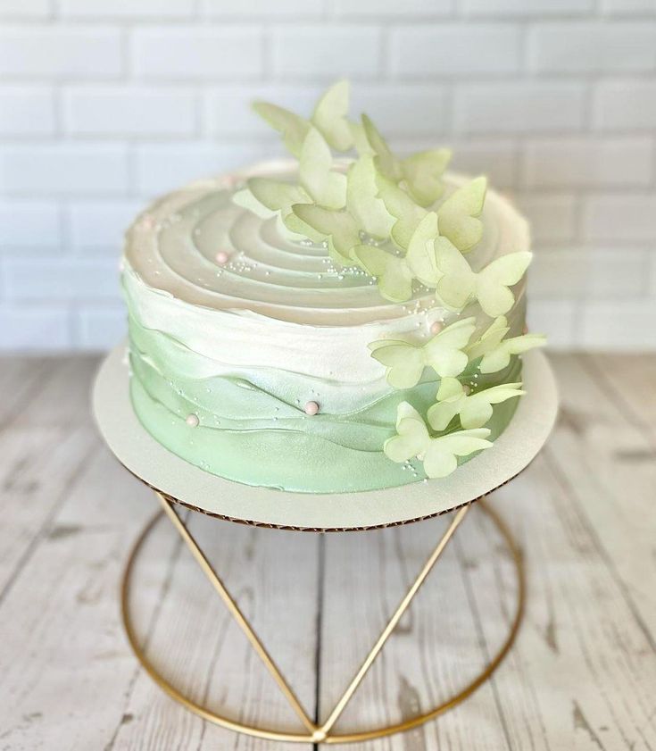 a cake sitting on top of a metal stand covered in frosting and green flowers