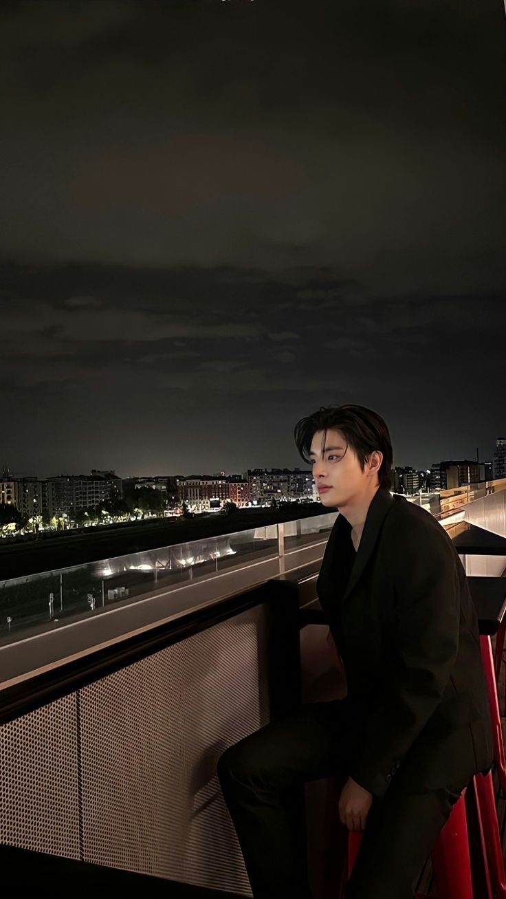 a man sitting on top of a red chair next to a railing near the ocean