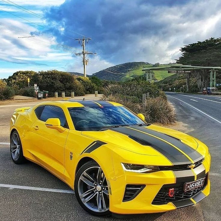 a yellow chevrolet camaro is parked in a parking lot next to a road and trees