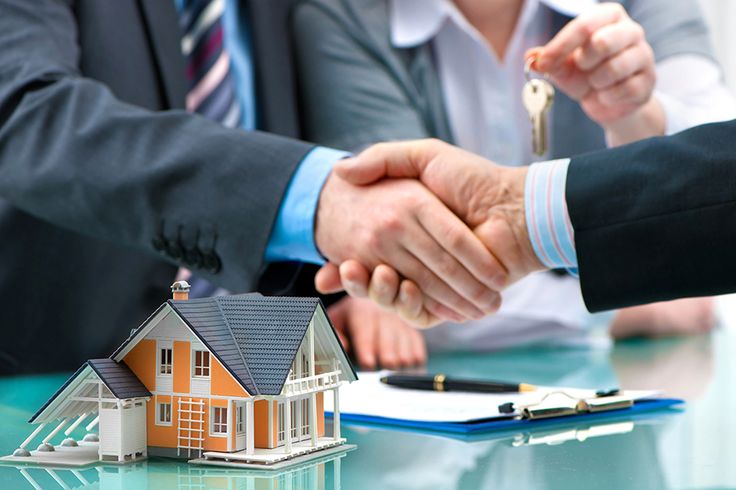 two people shaking hands over a house model on a table with keys in front of them