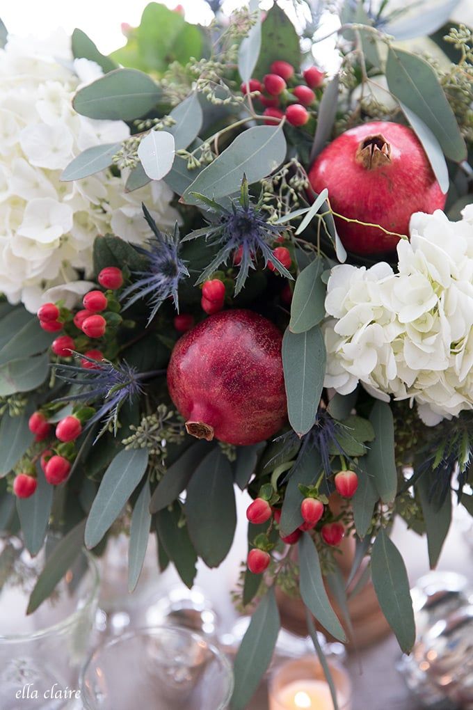 pomegranates and greenery are arranged in a vase on a table