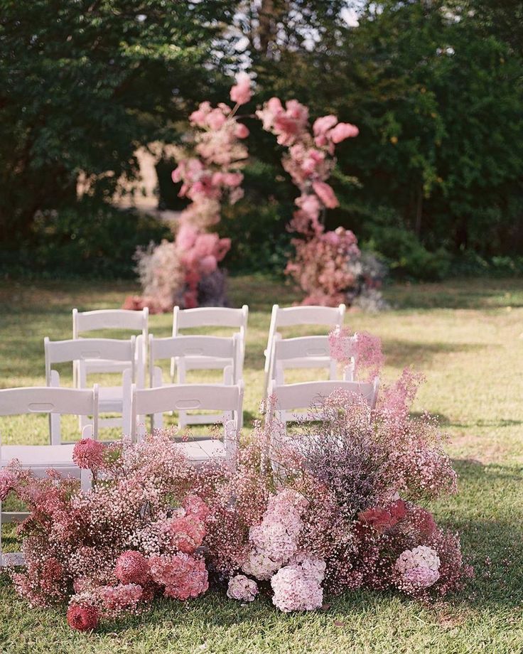 an outdoor ceremony setup with white chairs and pink flowers