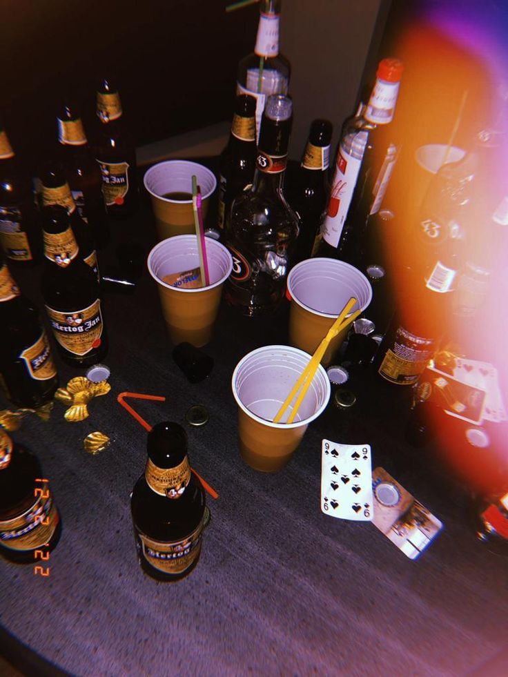 there are many bottles and cups on the table with playing cards in front of them